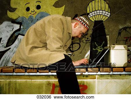 A man typing on a laptop in front of graffiti View Large Photo Image Stock Photograph - A man typing on a laptop in front of graffiti. Fotosearch