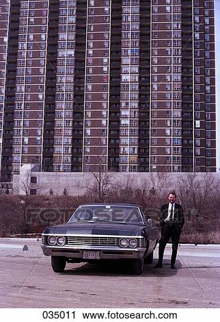 A man standing next to a car in front of an apartment building View Large Photo Image Stock Image - A man standing next to a car in front of an apartment building. Fotosearch