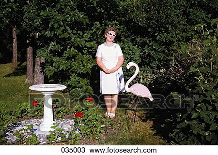 A woman standing in a garden next to a statue of a pink flamingo View Large Photo Image Stock Image - A woman standing in a garden next to a statue of a pink flamingo. Fotosearch