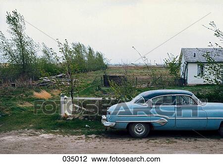 Stock Image - An old, blue car parked in front of a house in the countryside. Fotosearch
