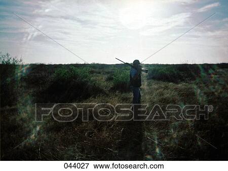 A person with a gun walking through a field View Large Photo Image Stock Photo - A person with a gun walking through a field. Fotosearch