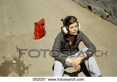 Stock Photo - A young woman listening to headphones while sitting on pavement. Fotosearch