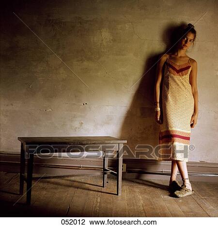 Stock Image - A young woman stands with her legs crossed by a small bench. Fotosearch