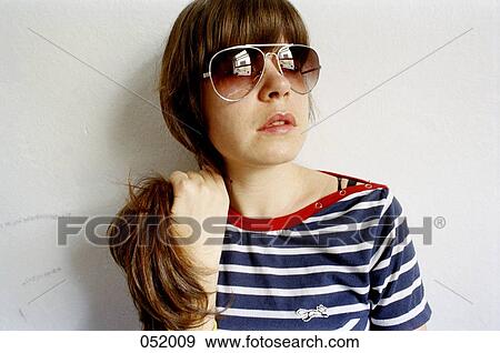 Stock Photo - A young woman wearing sunglasses holds her hair back. Fotosearch