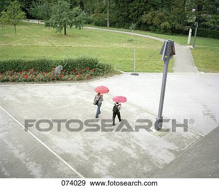 Two people walking with umbrellas View Large Photo Image Stock Photo - Two people walking with umbrellas. Fotosearch