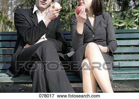A businessman and a businesswoman sitting on a park bench eating apples View Large Photo Image Stock Photo - A businessman and a businesswoman sitting on a park bench eating apples . Fotosearch