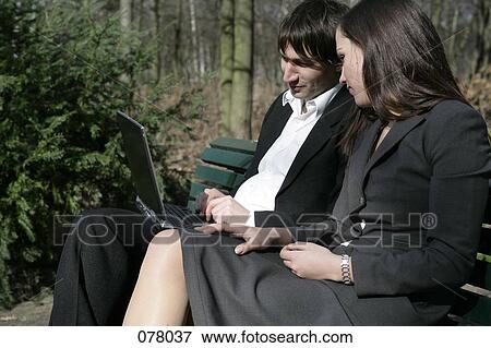A businessman and a businesswoman looking at a laptop computer on a park bench View Large Photo Image Stock Photo - A businessman and a businesswoman looking at a laptop computer on a park bench. Fotosearch