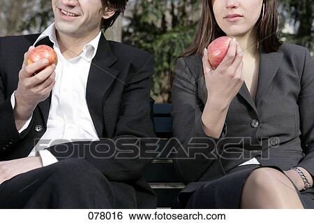 A businessman and a businesswoman holding apples while sitting on a bench View Large Photo Image Stock Photograph - A businessman and a businesswoman holding apples while sitting on a bench . Fotosearch