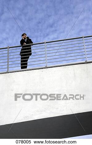 A businessman leaning on a railing with a mobile phone View Large Photo Image Stock Photography - A businessman leaning on a railing with a mobile phone. Fotosearch