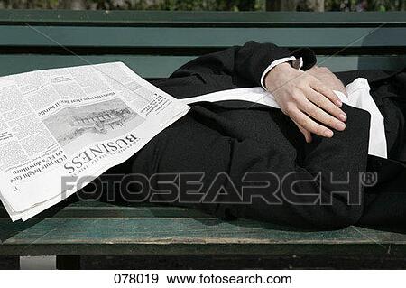 A businessman lying down on his back on a park bench with a newspaper covering his face View Large Photo Image Stock Photo - A businessman lying down on his back on a park bench with a newspaper covering his face. Fotosearch