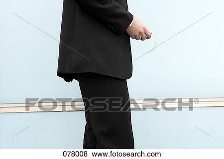 A businessman standing next to a wall holding a portable music player View Large Photo Image Stock Photo - A businessman standing next to a wall holding a portable music player. Fotosearch
