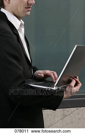 A businessman standing while typing on a laptop computer View Large Photo Image Stock Image - A businessman standing while typing on a laptop computer. Fotosearch