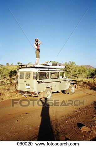 Stock Image - A woman taking a picture on top of an off-road vehicle, Australia. Fotosearch