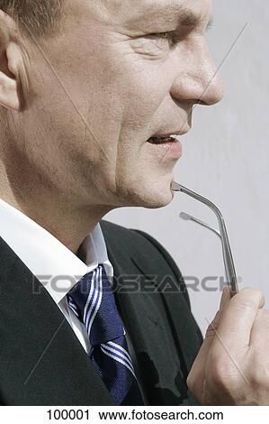 Stock Image - Businessman holding glasses near chin. Fotosearch
