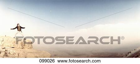 Stock Photograph - Man with arms outstretched standing on cliff, Israel. Fotosearch