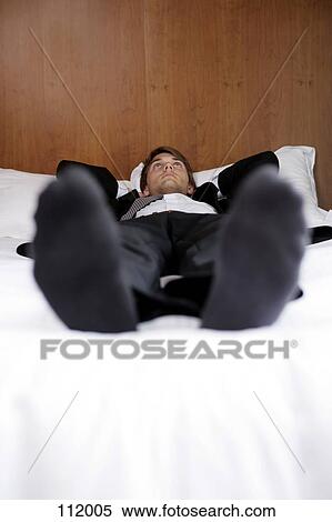 Stock Photography - Businessman lying down on bed. Fotosearch