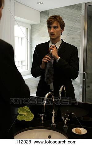 Man tying his necktie in the mirror View Large Photo Image Stock Photo - Man tying his necktie in the mirror. Fotosearch