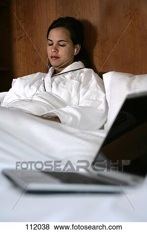 Woman in bed listening to headphones View Large Photo Image Stock Photo - Woman in bed listening to headphones. Fotosearch