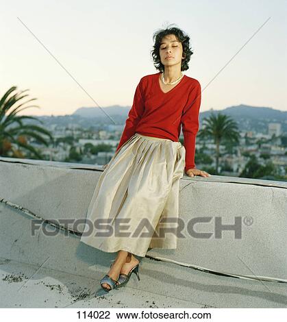 Stock Image - Woman sitting on ledge with eyes closed. Fotosearch