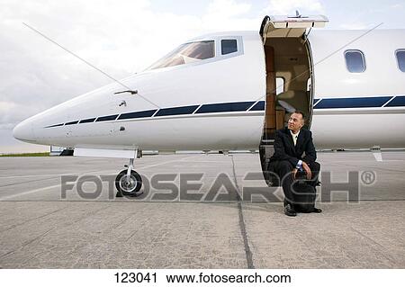 Stock Image - Businessman sitting on a private airplane’s steps. Fotosearch