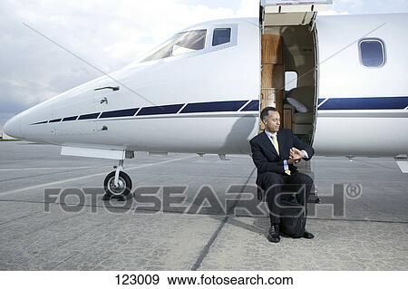 Stock Photo - Businessman sitting on a private airplane‘s steps. Fotosearch