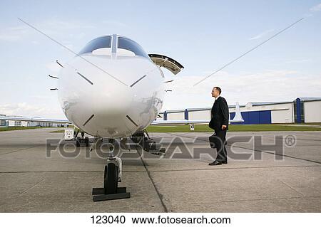Businessman standing next to an airplane View Large Photo Image Stock Image - Businessman standing next to an airplane. Fotosearch
