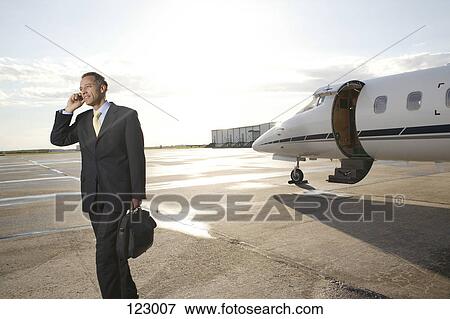 Businessman with cell phone standing near a private airplane View Large Photo Image Stock Photo - Businessman with cell phone standing near a private airplane. Fotosearch