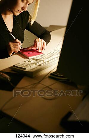 Picture - Woman holding pen, sitting at an office desk. Fotosearch