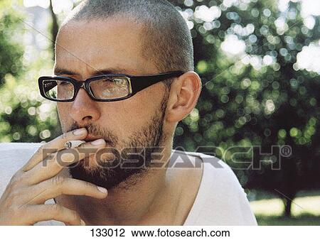 A man wearing glasses smoking a cigarette View Large Photo Image Stock Image - A man wearing glasses smoking a cigarette. Fotosearch
