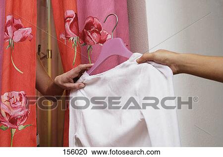 Stock Image - A person passing a shirt to another person in a changing room. Fotosearch