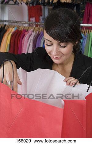 A woman smiling as she looks into a shopping bag View Large Photo Image Stock Photo - A woman smiling as she looks into a shopping bag. Fotosearch
