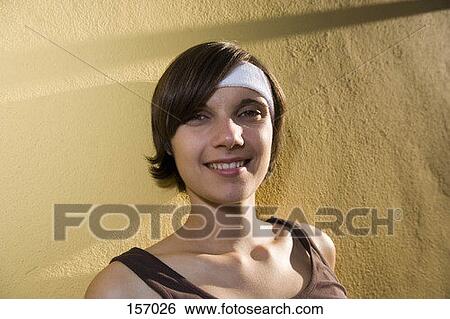 A young woman standing against a yellow wall, smiling View Large Photo Image Stock Photograph - A young woman standing against a yellow wall, smiling. Fotosearch