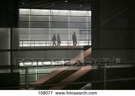 Three people walking in the corridor of a building View Large Photo Image Stock Photo - Three people walking in the corridor of a building. Fotosearch