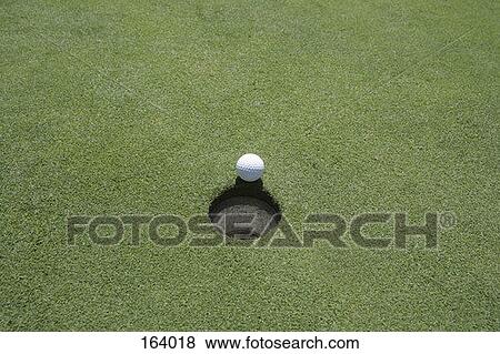 Stock Photo - High angle view of a golf ball at the edge of the hole. Fotosearch