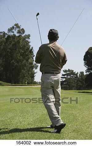 Stock Image - Rear view of a golfer after hitting a ball. Fotosearch