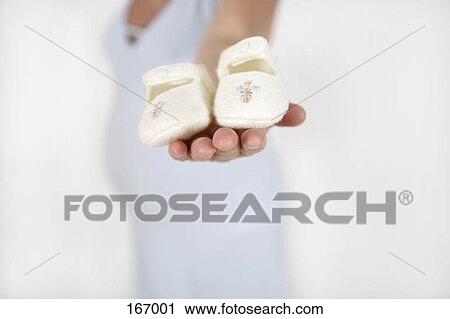 Stock Image - A pregnant woman holding baby shoes. Fotosearch