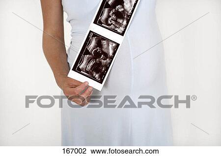 Stock Image - Midsection of a pregnant woman holding ultrasound images. Fotosearch