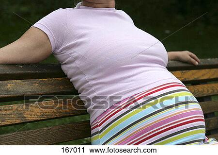 Stock Image - Midsection of a pregnant woman sitting on a park bench. Fotosearch