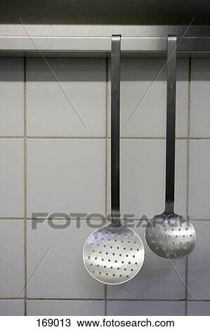 Stock Image - Front view of two strainers hanging in a kitchen. Fotosearch