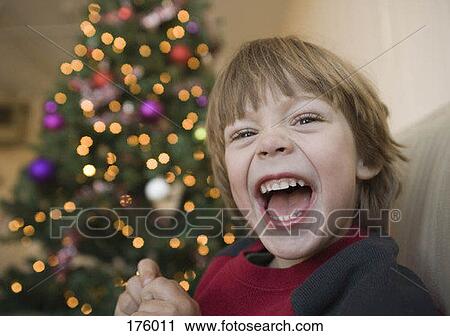 Stock Image - A young boy laughing in front of a Christmas tree. Fotosearch