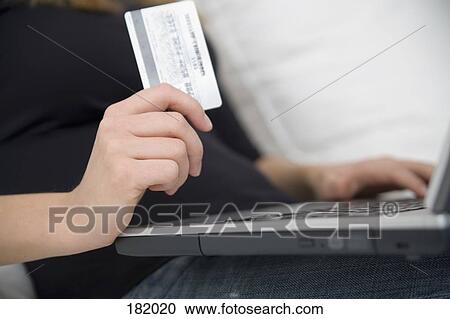 Stock Image - Young woman holding credit card and using laptop. Fotosearch