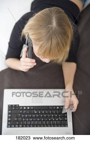 Young woman holding credit card and telephone while lying down in front of laptop View Large Photo Image Stock Image - Young woman holding credit card and telephone while lying down in front of laptop. Fotosearch