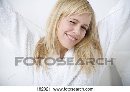 Stock Image - Young woman in bathrobe stretching arms. Fotosearch