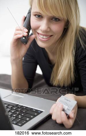 Young woman lying on front holding telephone and credit card and using laptop View Large Photo Image Stock Photograph - Young woman lying on front holding telephone and credit card and using laptop. Fotosearch