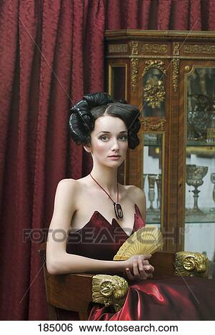 Stock Photograph - Elegant young woman seated in red ball gown. Fotosearch
