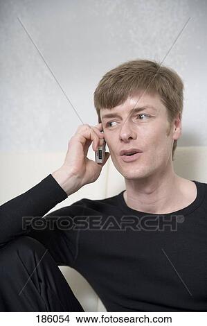 Man sitting on sofa and talking on mobile phone View Large Photo Image Picture - Man sitting on sofa and talking on mobile phone. Fotosearch