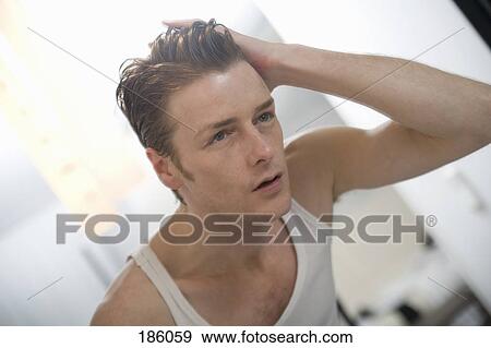 Stock Photo - Man standing in front of mirror with hand in hair. Fotosearch