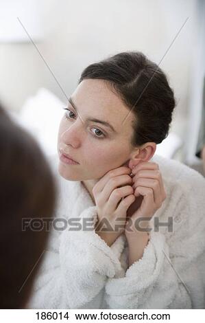 Woman putting earring on in front of mirror View Large Photo Image Picture - Woman putting earring on in front of mirror. Fotosearch