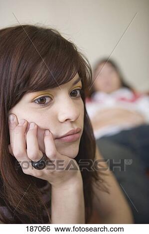 Teenage girl looking away while teenage boy sits in background View Large Photo Image Stock Photograph - Teenage girl looking away while teenage boy sits in background. Fotosearch