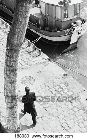 Man walking along riverbank near docked motorboat View Large Photo Image Stock Image - Man walking along riverbank near docked motorboat. Fotosearch